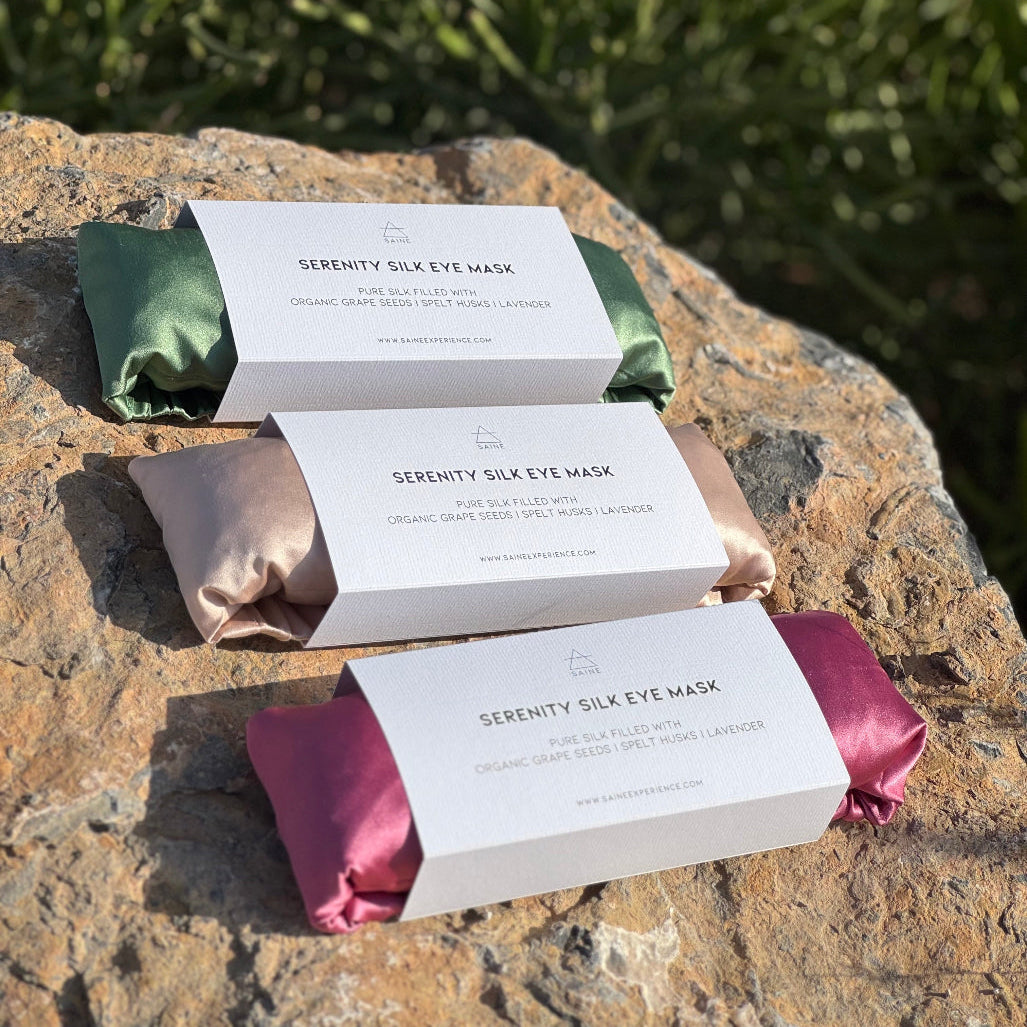Serenity Silk Eye Mask packaging on a stone surface with greenery in the background